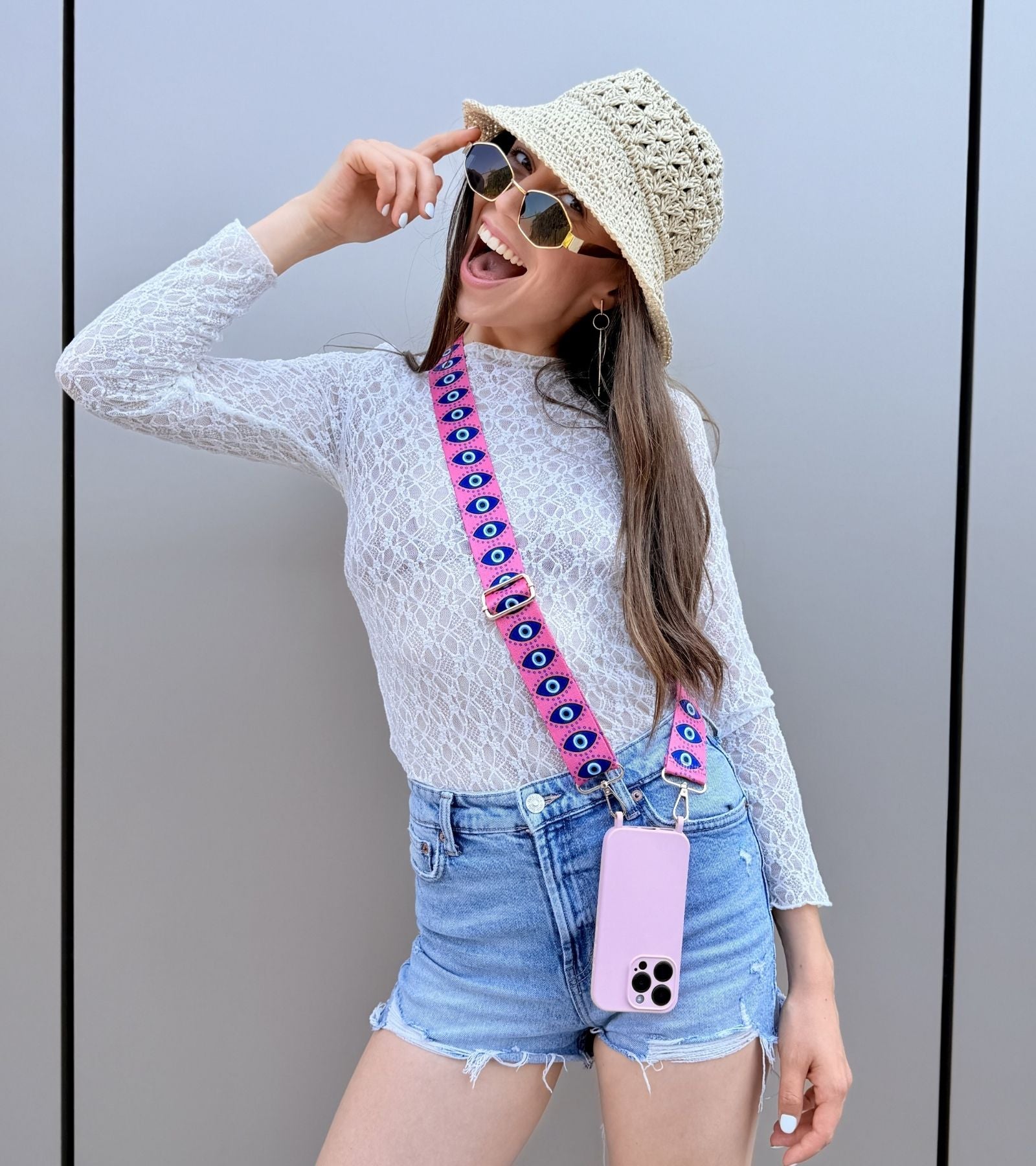 Strappy Set Art Evil Eye na modelke – ružový crossbody popruh na mobil s motívom Evil Eye a fialový kryt na iPhone ako súčasť letného outfitu.