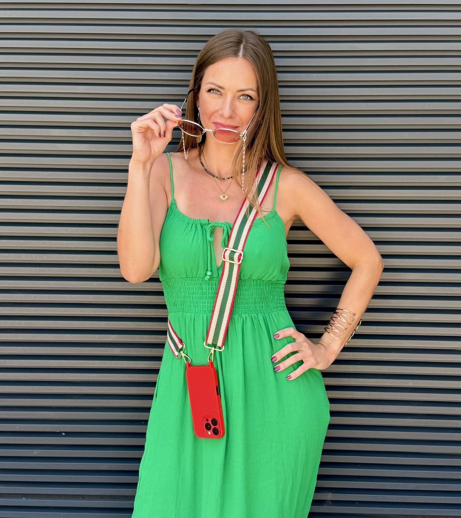 Strappy Set Retro Forest Green na modelke – retro pásikavý crossbody popruh na mobil v zeleno-béžovo-červenej farebnej kombinácii a červený kryt na iPhone ako súčasť outfitu.