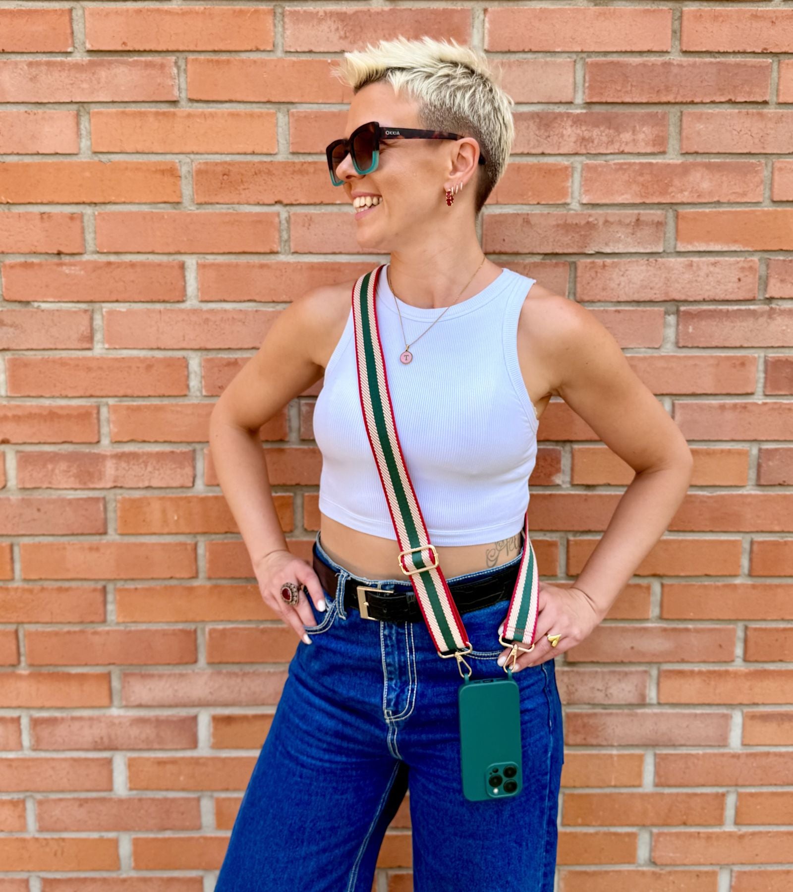 Strappy Set Retro Forest Green na modelke – retro pásikavý crossbody popruh na mobil v zeleno-béžovo-červenej farebnej kombinácii a tmavozelený kryt na iPhone ako štýlový módny doplnok.