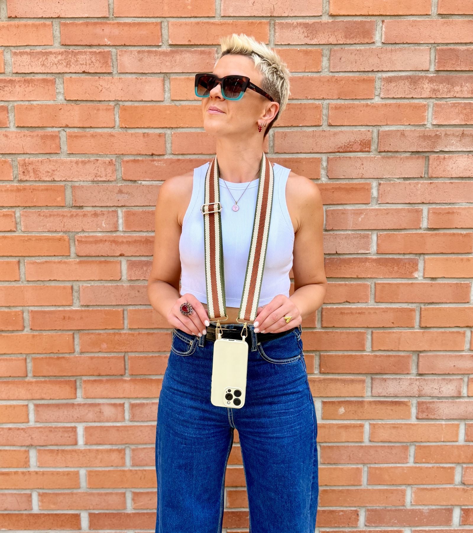 Strappy Set Retro Vintage Brown na modelke – retro pásikavý crossbody popruh na mobil v hnedej farebnej kombinácii a béžový kryt na iPhone pre voľné ruky počas dňa.
