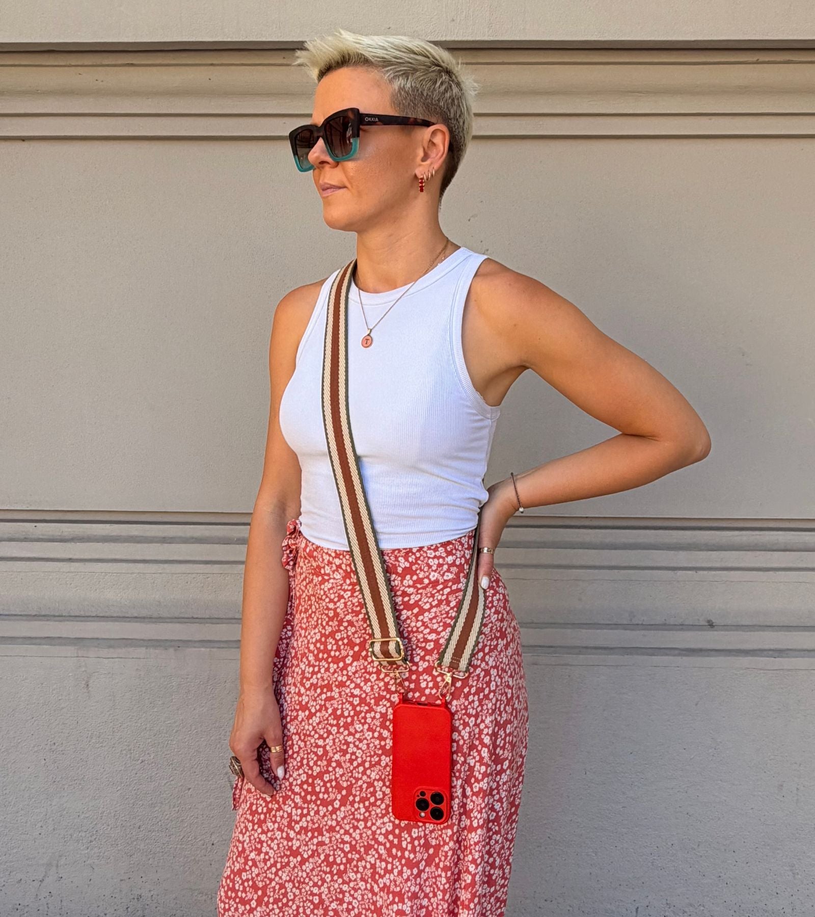 Strappy Set Retro Vintage Brown na modelke – retro pásikavý crossbody popruh na mobil v hnedej farebnej kombinácii a červený kryt na iPhone ako súčasť outfitu.